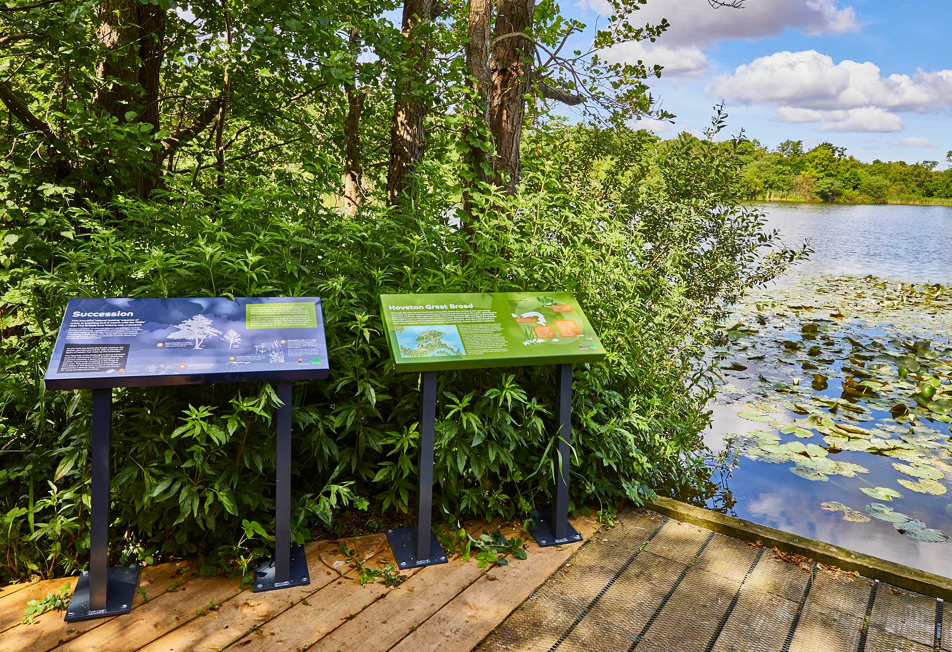 Two interpretation panels at Hoveton Broad, fixed to timber decking on a sunny day